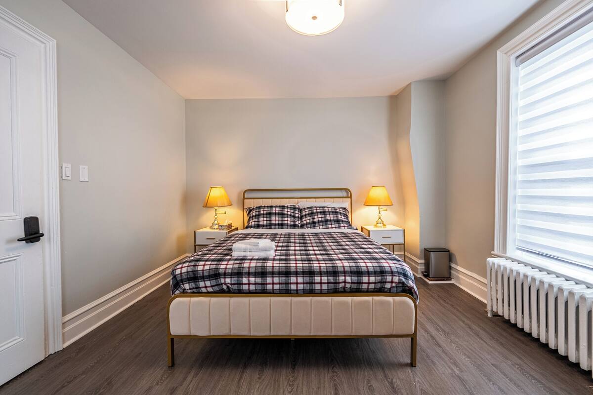A neatly arranged bedroom with a bed, two bedside tables with lamps, a radiator, and a door.