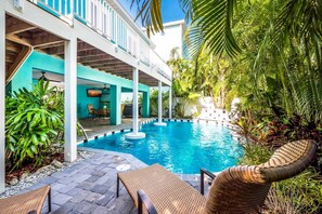 Un espace piscine doté de chaises longues, d’un coin salon abrité et d’une végétation tropicale luxuriante.