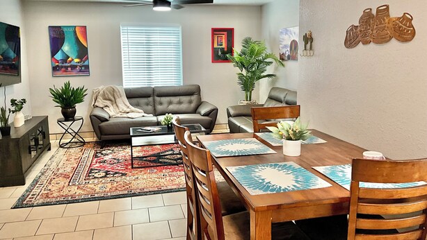 A living room with a sofa, coffee table, dining table, chairs, and a ceiling fan.