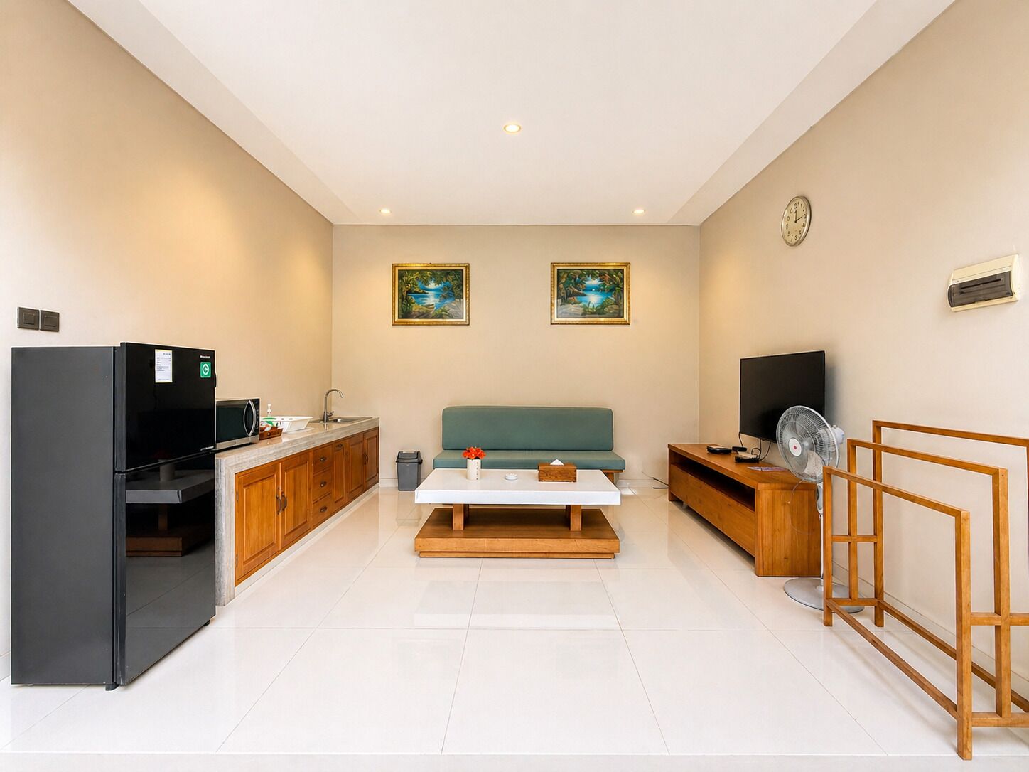 A compact living space with a kitchenette, a sofa, a TV, and a fan.