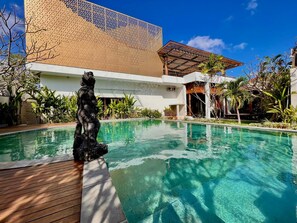 A pool with a statue, surrounded by tropical plants and a modern building with a geometric facade. - D'Avera Villa (Canggu)