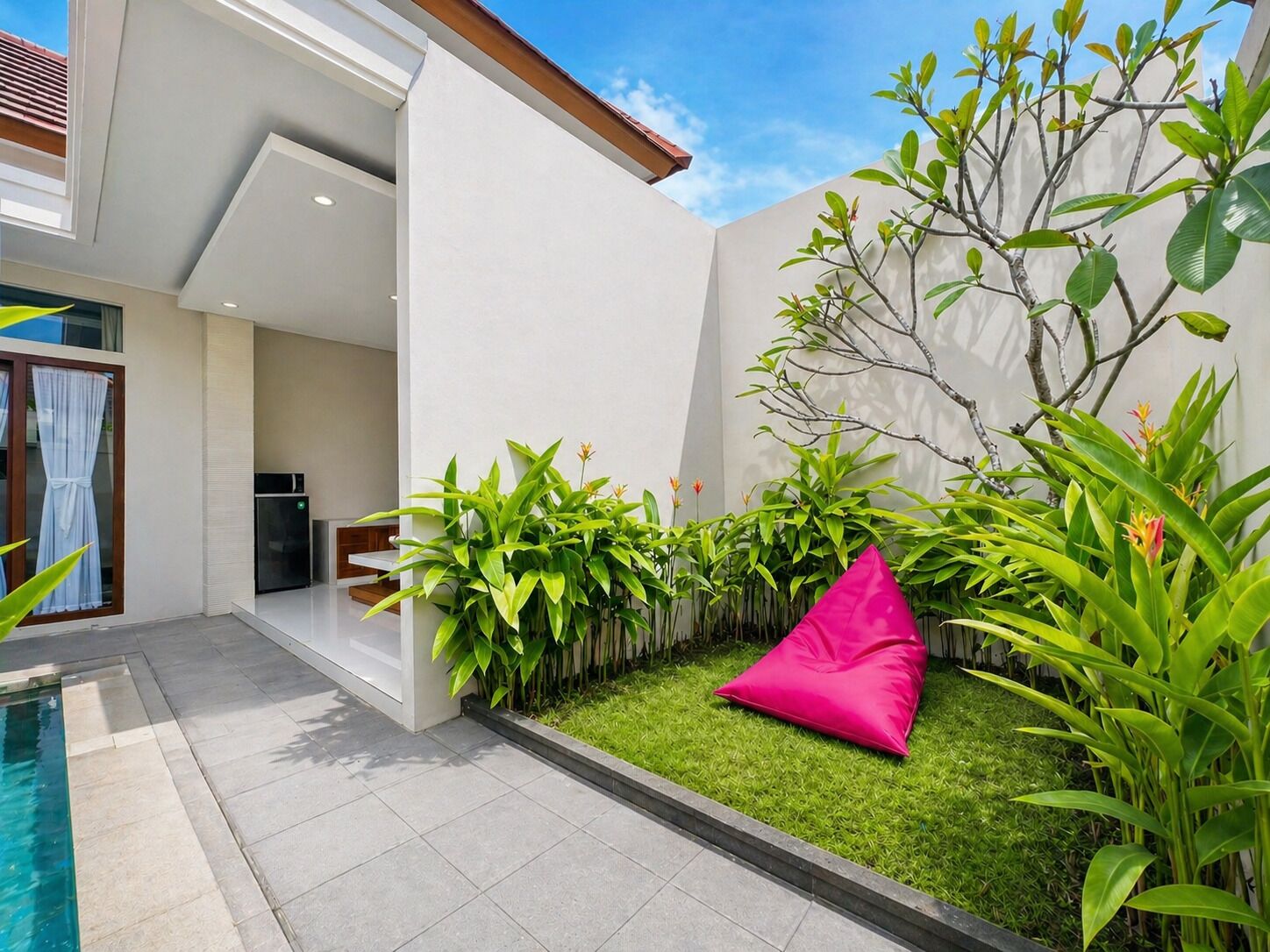 Ein moderner Außenbereich mit Pool, einer Sitzecke mit rosa Kissen und üppigem Grün.