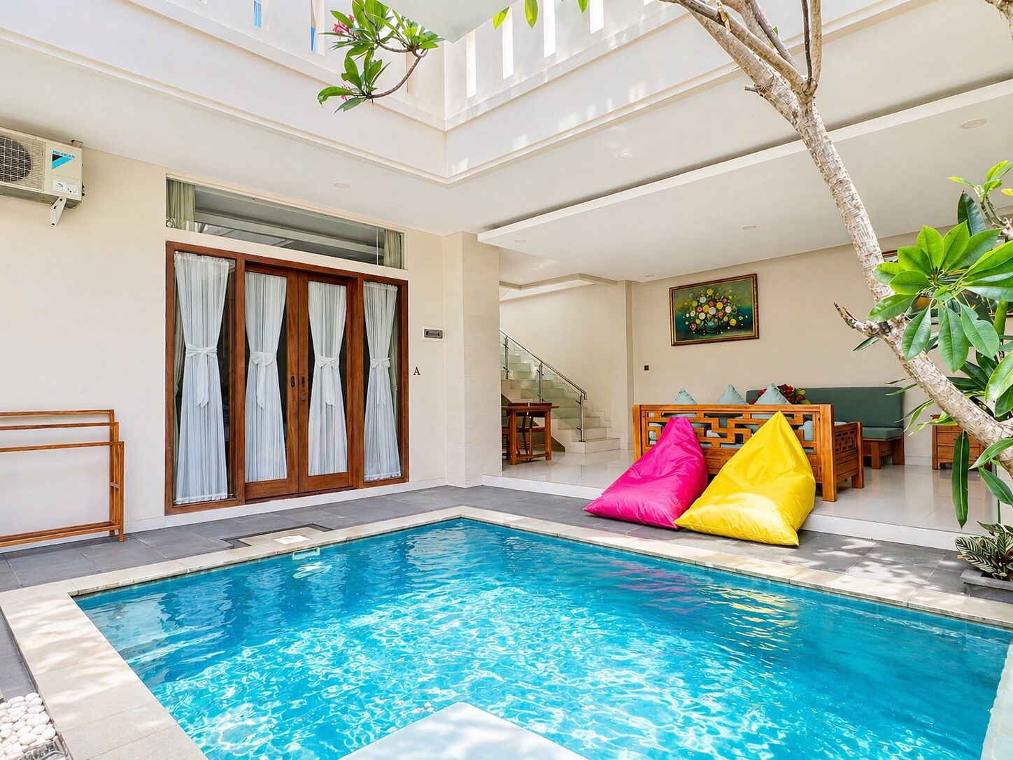 A swimming pool with a wooden deck, a staircase, and a dining area with a green sofa and colorful cushions.