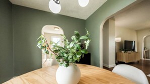 Ein Essbereich mit einem runden Holztisch, einer weißen Vase mit Grünpflanzen und einem Fernseher im Hintergrund.