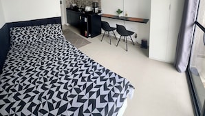 Una habitación de hotel moderna con una cama grande, una kitchenette, un televisor y un ventanal con cortinas.