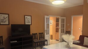 A living room with a television, chairs, a coffee table, and a door leading to another room.
