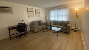 Ein Wohnzimmer mit einer Couch, einem Couchtisch, einem Schreibtisch mit Stuhl und einer Stehlampe.