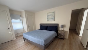 Ein Schlafzimmer mit einem Bett, einem Nachttisch, einer Tür und einem Bild an der Wand.