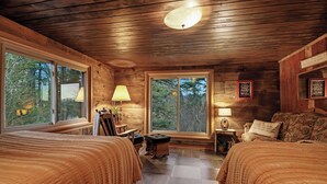 Un dormitorio acogedor en una cabaña, con dos camas, paredes de madera, ventanas grandes y una lámpara en el techo.
