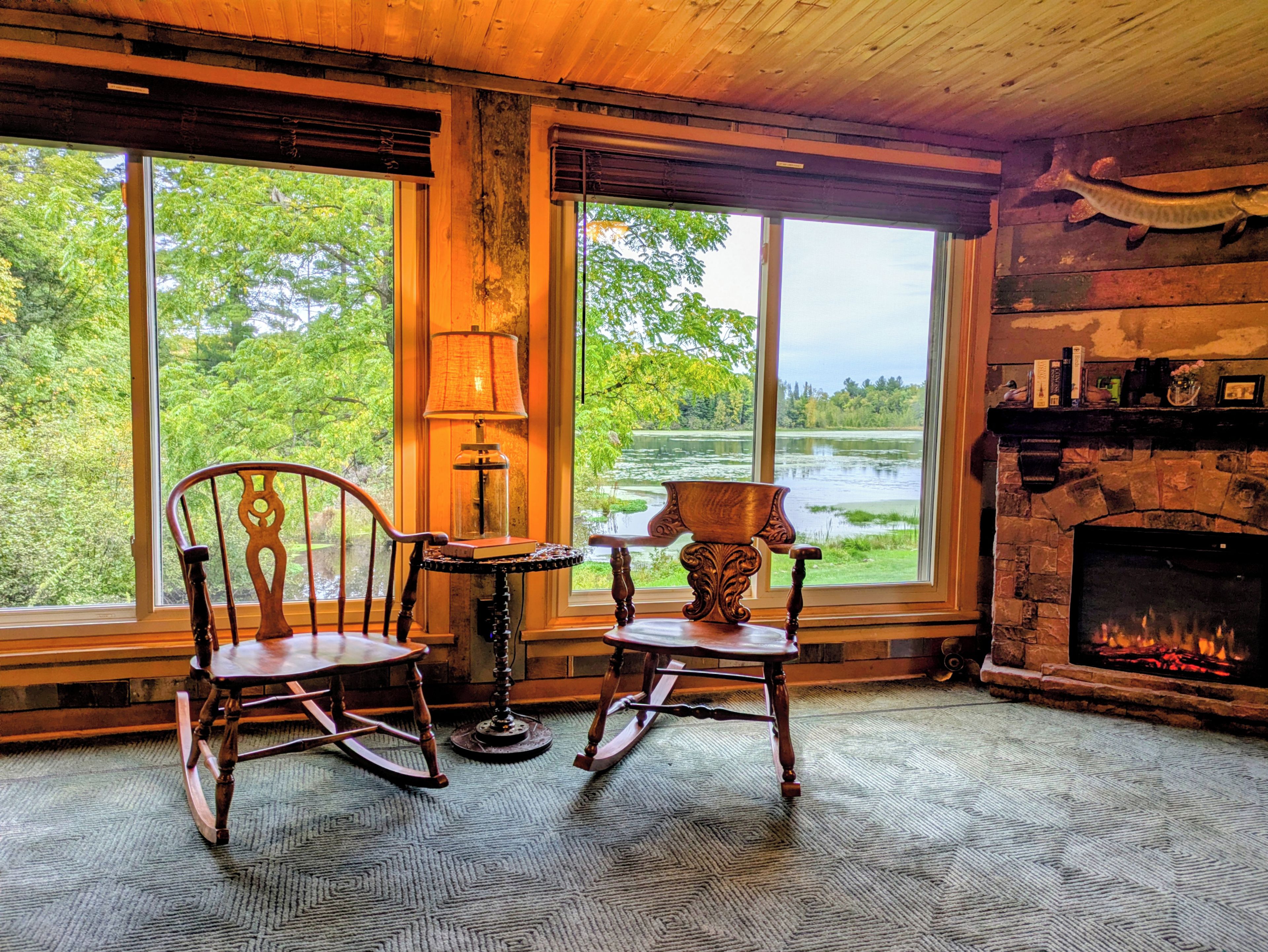 A room with two rocking chairs, a fireplace, and a view of a lake through large windows.