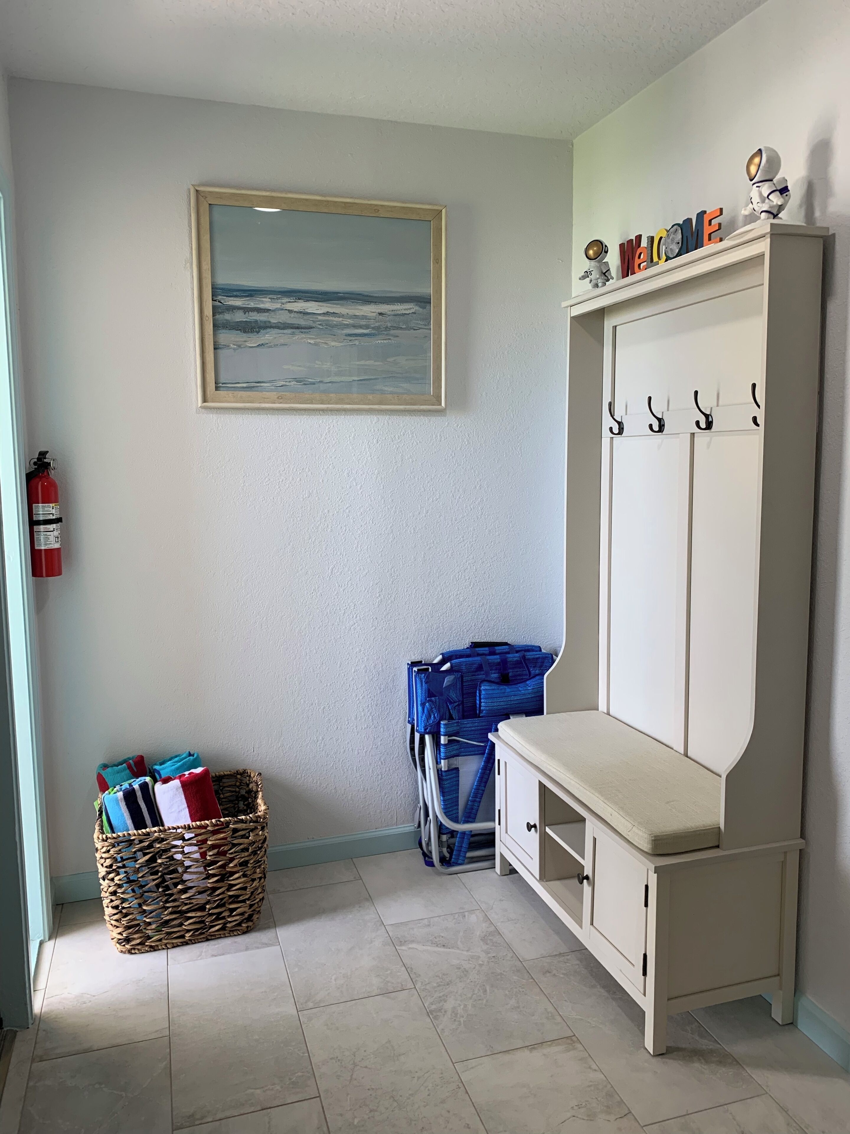 A room with a framed painting, a fire extinguisher, a wicker basket, a blue stroller, and a white wardrobe with hooks.