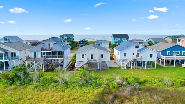 Una zona residenziale sulla costa, con case dotate di balconi e terrazze, alcune con garage integrati, e vista libera sull'oceano.