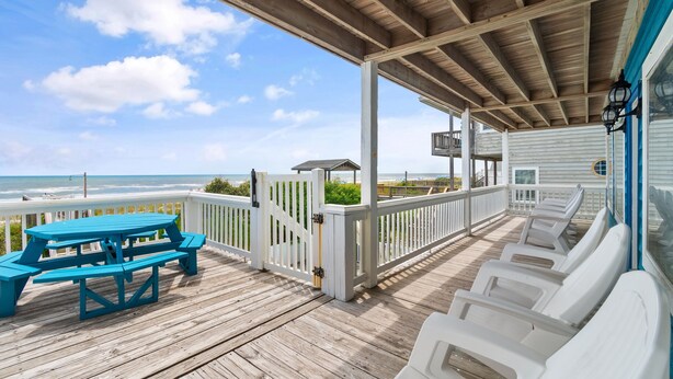 A wooden deck with a picnic table and lounge chairs, overlooking the ocean.