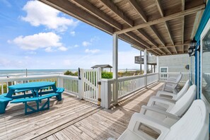 A wooden deck with a picnic table and lounge chairs, overlooking the ocean.