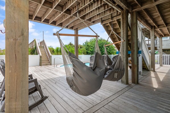 A wooden deck with hammocks and a pool in the background.