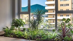 Une pièce dotée d’une grande fenêtre, agrémentée de plantes en pot, et offrant une vue sur une montagne et des bâtiments.