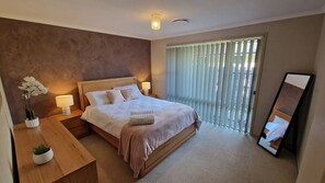 A neatly arranged bedroom with a large bed, bedside tables, a mirror, and a window with blinds.