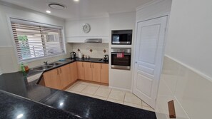 A modern kitchen with a black countertop, wooden cabinets, a stainless steel range hood, a microwave, and a double oven.