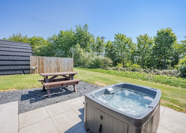 A backyard with a hot tub, picnic table, and a wooden fence.