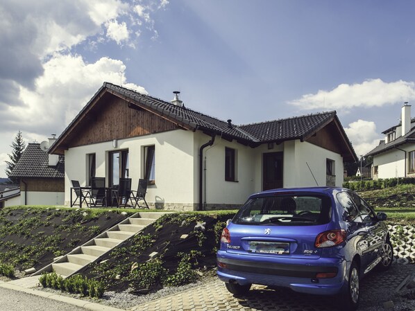 Una casa moderna con tetto spiovente, un'auto parcheggiata nel vialetto e una scalinata che conduce all'ingresso.