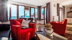 Una sala de estar moderna con sofás rojos, una mesa de centro de madera y ventanas grandes con vistas al mar.