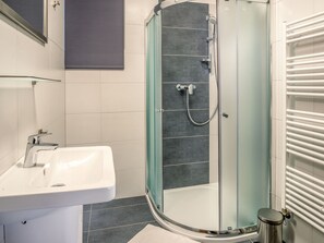 Une salle de bain moderne avec une douche à parois de verre, un lavabo blanc et un sol carrelé.