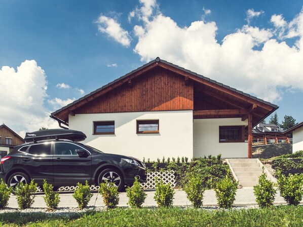 Une maison moderne à deux étages, avec une voiture garée devant.