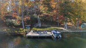 Eine Anlegestelle mit einem überdachten Boot, einer Steinmauer und einer Rasenfläche mit Adirondack-Stühlen.