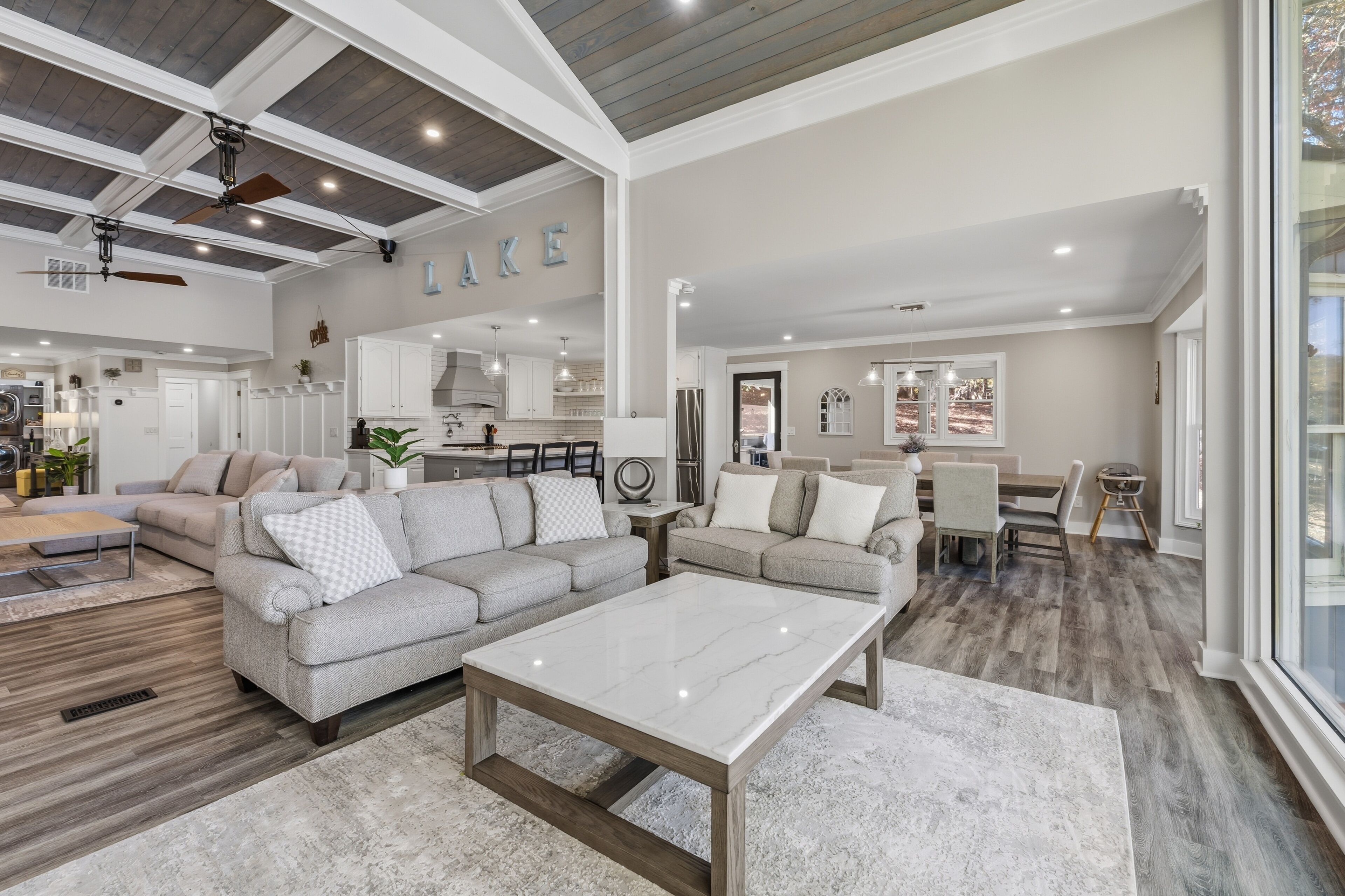 A spacious living room with a large sectional sofa, a marble coffee table, and a dining area with a wooden table and chairs.