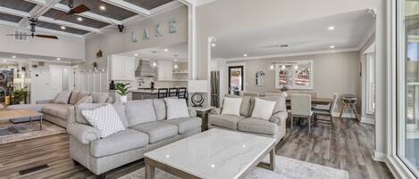 A spacious living room with a large sectional sofa, a marble coffee table, and a dining area with a wooden table and chairs.
