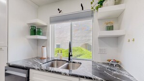 A kitchen with a marble countertop, stainless steel sink, white cabinets, and a window with a view of greenery. - Contemporary Monochrome Retreat With 4beds & POOL (Albuquerque)