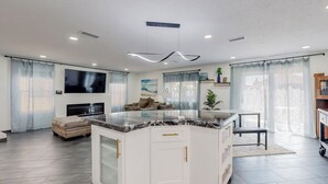 A modern kitchen with a central island, white cabinetry, and a large window with sheer curtains. - Contemporary Monochrome Retreat With 4beds & POOL (Albuquerque)