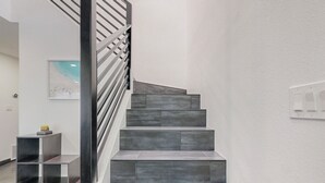 A modern staircase with grey steps and a metal railing, leading to a landing with a small shelf and a framed picture on the wall. - Contemporary Monochrome Retreat With 4beds & POOL (Albuquerque)