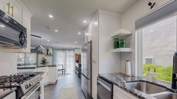 A modern kitchen with white cabinetry, stainless steel appliances, and a large window offering a view of greenery. - Contemporary Monochrome Retreat With 4beds & POOL (Albuquerque)