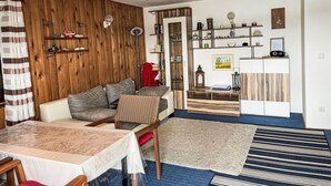 A cozy living room with a sofa, a dining table, and a kitchen area with cabinets and shelves. - Bootshaus auf dem See by Interhome (Lindow)