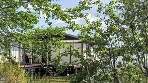 A modern house with a deck extending over water, surrounded by lush greenery. - Bootshaus auf dem See by Interhome (Lindow)