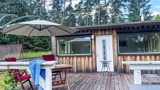 A wooden deck with a table and chairs, a door, and large windows. - am Pälitzsee by Interhome (Rheinsberg)