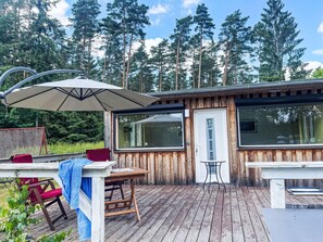 A wooden deck with a table and chairs, a door, and large windows.