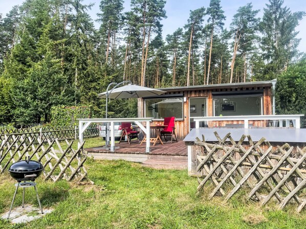 A wooden cabin with a deck, a barbecue grill, and a red chair.