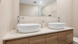 Een badkamer met twee witte wasbakken, een houten kastje en een spiegel boven de wasbakken.
