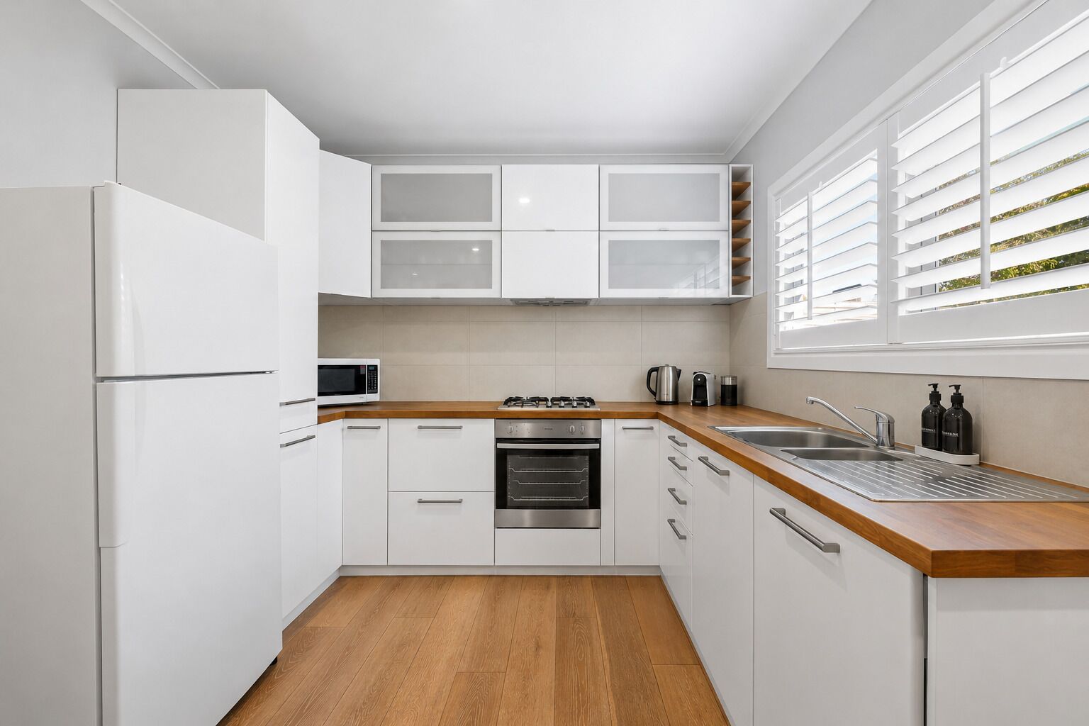 A modern kitchen with white cabinets, a wooden countertop, a built-in oven, a microwave, and a sink.