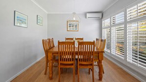 Een eetkamer met een houten tafel en stoelen, een hanglamp en een raam met jaloezieën.