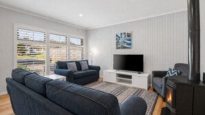 Een woonkamer met een bank, televisie, open haard en uitzicht door grote ramen.