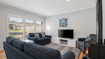 A living room with a sofa, TV, fireplace, and a view through large windows.