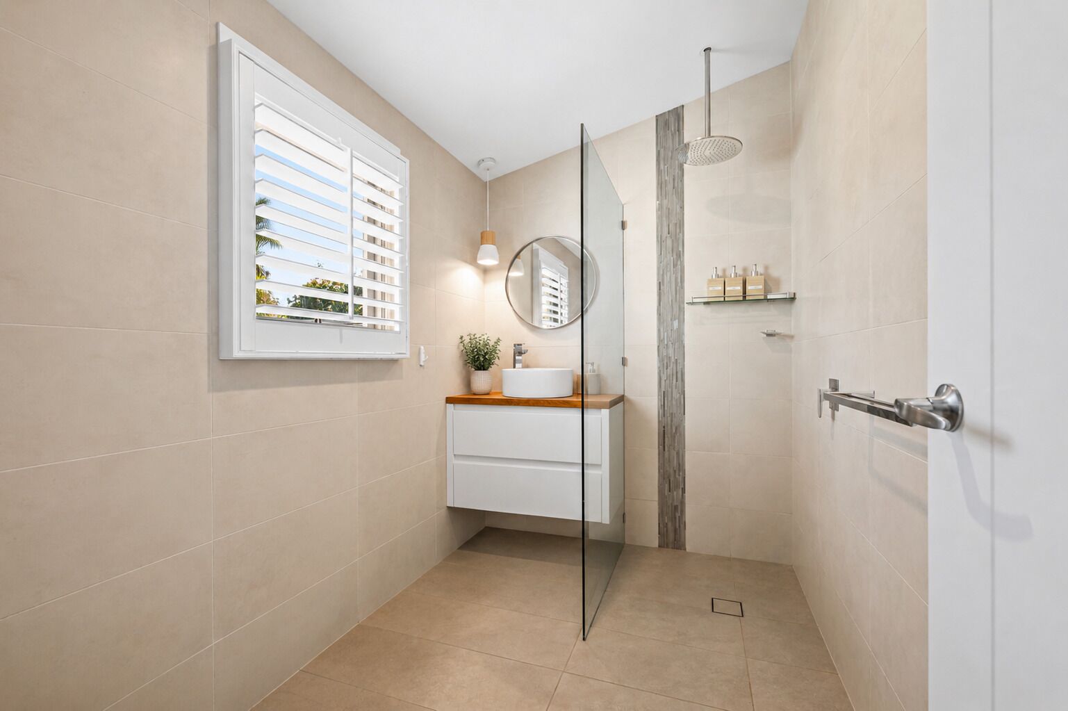 A bathroom with a glass shower door, a sink with a mirror, and a window with blinds.