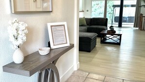 Una sala de estar moderna con una mesa consola de madera oscura, un cuadro enmarco y un jarrón con flores blancas.