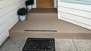 Una entrada principal con puerta de madera, plantas en macetas y ventana con persianas.