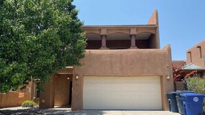 A stucco house with a white garage door, a covered balcony, and a tree in the driveway. - Amazing 4-bedroom: AC, WiFi, 2 car garage with river view in NW Albuquerque (Albuquerque)