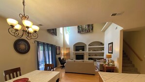 A spacious living area with a dining table, sofa, and a TV mounted above a fireplace. - Amazing 4-bedroom: AC, WiFi, 2 car garage with river view in NW Albuquerque (Albuquerque)