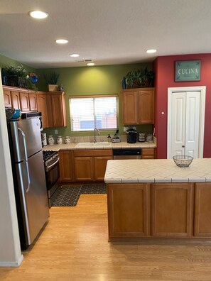 A kitchen with wooden cabinets, a stainless steel refrigerator, a sink, and a window with blinds. - Amazing 4-bedroom: AC, WiFi, 2 car garage with river view in NW Albuquerque (Albuquerque)